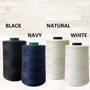 May include: Four spools of thread in black, navy, natural, and white. Each spool is cylindrical with a black or green top. The words "BLACK", "NAVY", "NATURAL", and "WHITE" are printed above each spool.