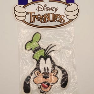 May include: A Disney Treasures patch featuring Goofy in a white, black, green, and tan design. The patch is in a clear plastic bag with a blue and white Disney Treasures header. The Disney logo is visible on the header and the patch.