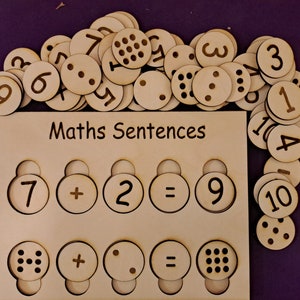 May include: Wooden board with cutouts for numbers and symbols, labelled "Maths Sentences". The board has two rows of cutouts, each with a number, a plus sign, a number, an equals sign, and a number. There are also wooden circles with numbers and dots on them.