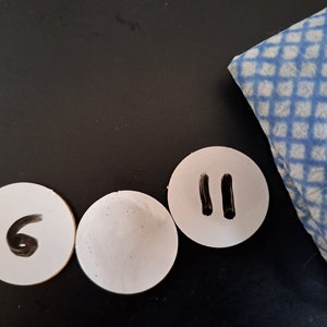 May include: Three white round paper circles with black markings. The left circle has the number "6" written on it. The middle circle is blank. The right circle has two vertical lines drawn on it.