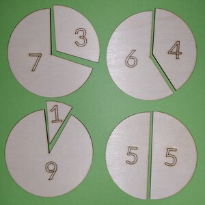Könnte beinhalten: Vier weiße Holzkreise, die in Abschnitte mit darauf geschriebenen Zahlen unterteilt sind. Die Zahlen sind 1, 3, 4, 5, 6, 7, 9. Die Kreise befinden sich auf einem grünen Hintergrund.