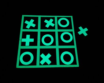 May include: A glow-in-the-dark tic-tac-toe game board with green circles and crosses. The board is made of a dark material and the symbols are bright green.