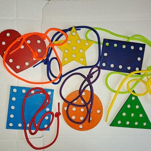 May include: A set of colourful wooden shapes with holes for lacing. The shapes include a heart, star, square, circle, and triangle. Each shape has a different colour and is made of wood. The shapes are designed for children to practise their fine motor skills and hand-eye coordination.