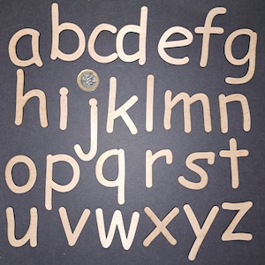 Peut inclure: Un ensemble de 26 lettres en bois minuscules, peintes en brun clair. Les lettres sont disposées en ordre alphabétique sur un fond gris foncé.