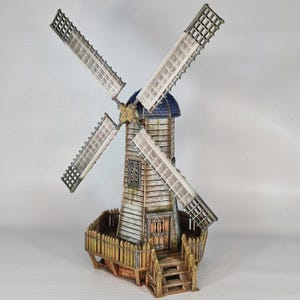 May include: A miniature wooden windmill with white sails and a blue roof. The windmill has a fence around the base and a set of stairs leading up to the door.