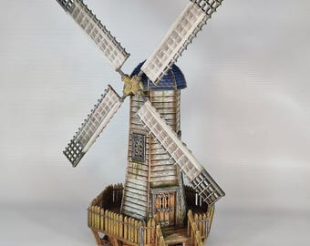 May include: A miniature wooden windmill with white sails and a blue roof. The windmill has a fence around the base and a set of stairs leading up to the door.