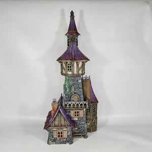 May include: A miniature stone tower with a purple roof and a smaller stone building attached. The tower has a pointed roof and several windows. The building has a brown roof and a single window.