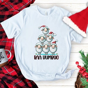 May include: A light blue t-shirt featuring a graphic of a stack of sheep wearing Santa hats. The text "Bah Humbug" is printed below the sheep.