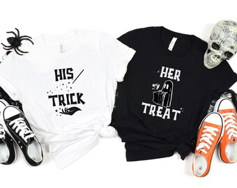 May include: Two white t-shirts with black text. One shirt says "His Trick" with a wand and stars. The other shirt says "Her Treat" with a ghost holding a bag of candy.