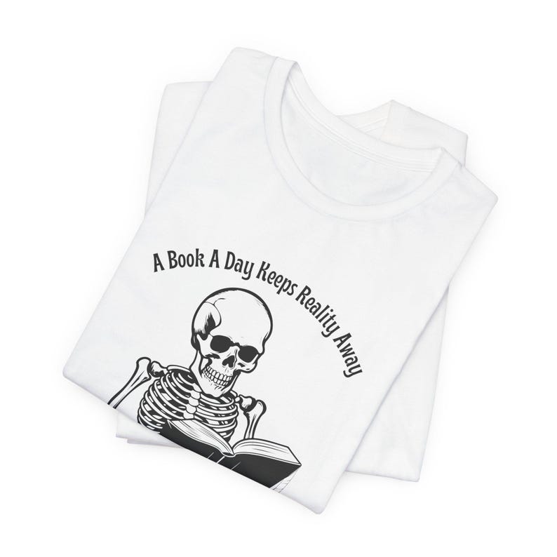 May include: White t-shirt with a black skeleton reading a book. The text on the shirt reads "A Book A Day Keeps Reality Away."