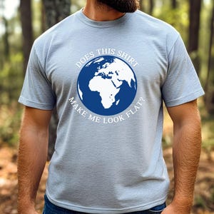 Peut inclure: Un t-shirt bleu clair avec un graphique blanc d'un globe terrestre et le texte "Does this shirt make me look flat?"