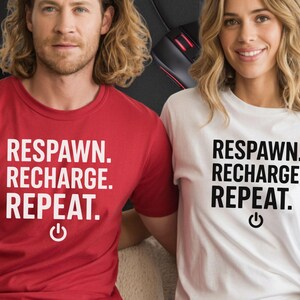 May include: Two t-shirts, one red and one white, each bearing the text "RESPAWN. RECHARGE. REPEAT." in a bold font. A power button graphic is below the text. The t-shirts are being worn by two people.