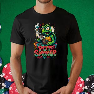 May include: Black t-shirt featuring a cartoon turtle smoking a cigarette and playing poker. The turtle is green and yellow, with the text "POT SMOKER" in colorful letters. The design includes poker chips and playing cards.
