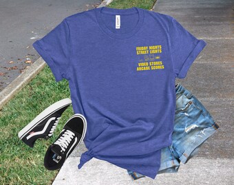 May include: A blue t-shirt with the text "FRIDAY NIGHTS STREET LIGHTS VIDEO STORES ARCADE SCORES" in yellow. The shirt is paired with black and white sneakers and denim shorts.