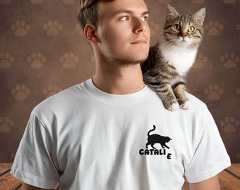 May include: A white t-shirt with a black cat silhouette and the word "CATALIZE" printed on the front. A tabby cat is sitting on the person's shoulder.