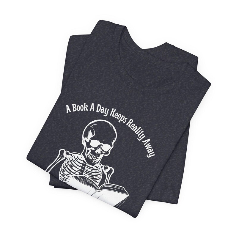 May include: A dark blue t-shirt with a white skeleton reading a book. The text on the shirt reads "A Book A Day Keeps Reality Away".