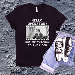 May include: Black t-shirt with a white graphic of a man on the phone with the text "Hello, Operator? Put me through to the moon."
