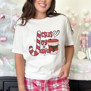 May include: White t-shirt featuring a red and white candy cane, a coffee cup with a red and green holly design, and the text "Jesus Joy & Java".