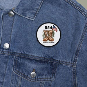 May include: A round patch with a military theme, featuring brown combat boots, an American flag, and the letters "RSW." The patch also includes a date. The patch is set against a denim jacket.