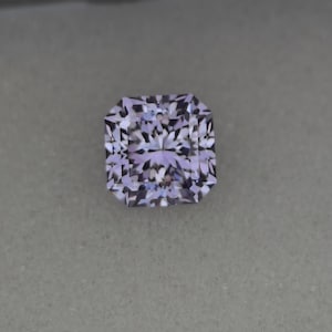 Può includere: Una pietra preziosa sfaccettata di forma quadrata con una tonalità viola e un centro bianco. La pietra preziosa presenta un motivo complesso a forma di stella all'interno delle sue sfaccettature.