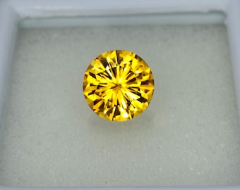May include: A round, faceted, yellow gemstone with a starburst pattern in the center. The gemstone is set in a white box.