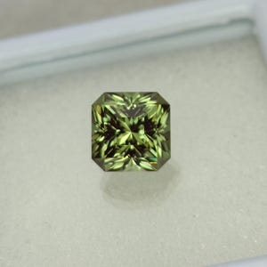 May include: A green gemstone with a square cut and a star-like pattern in the center.