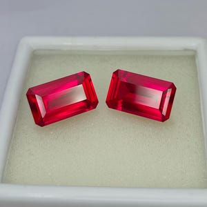 May include: Two vibrant red emerald-cut gemstones, set against a white background.
