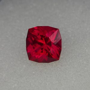 Può includere: Una pietra preziosa di colore rosso intenso con forma quadrata e molte sfaccettature.