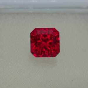 May include: A deep red gemstone with a square shape and a faceted cut.