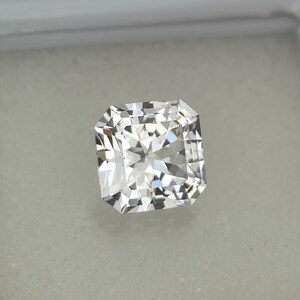 Puede incluir: Un diamante incoloro de talla radiante, de forma cuadrada y facetada. La gema se presenta sobre un fondo neutro, resaltando su brillo y claridad. Este diamante es un s&iacute;mbolo de lujo y elegancia.