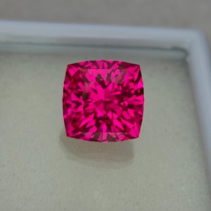 Puede incluir: Una gema rosa vibrante con un corte de cojín y un diseño facetado.