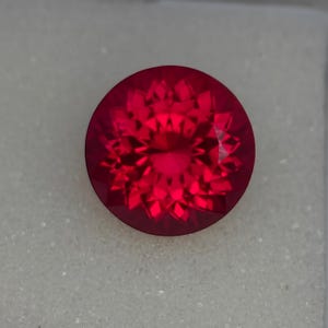 May include: A deep red gemstone with a faceted cut, showcasing a star-like pattern in the centre.