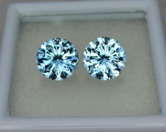May include: Two round, light blue gemstones with a faceted cut. The gemstones are displayed in a white box.