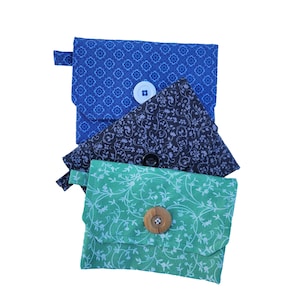 May include: Three fabric pouches with different patterns and button closures. The top pouch is blue with a white button, the middle pouch is black with a white button, and the bottom pouch is green with a wooden button.