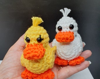 May include: Two crocheted duck plushies, one yellow with orange beak and feet, the other white with orange beak and feet.