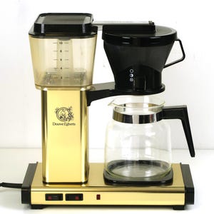 May include: A gold and black coffee maker with a transparent water reservoir featuring markings from 2 to 10. The machine includes a black filter basket, a glass carafe with a black handle, and a base with two black switches and the Douwe Egberts logo.