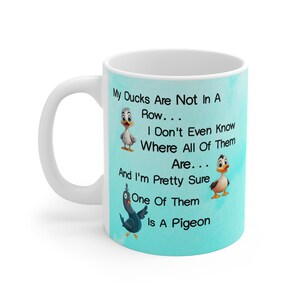 May include: White ceramic mug with a light blue background featuring a cartoon illustration of ducks and a pigeon. The text on the mug reads: "My Ducks Are Not In A Row... I Don't Even Know Where All Of Them Are... And I'm Pretty Sure One Of Them Is A Pigeon."