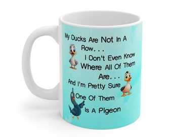 May include: White ceramic mug with a light blue background featuring a cartoon illustration of ducks and a pigeon. The text on the mug reads: "My Ducks Are Not In A Row... I Don't Even Know Where All Of Them Are... And I'm Pretty Sure One Of Them Is A Pigeon."