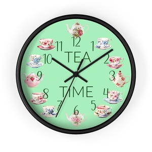 May include: Round wall clock with a black frame and a light green face. The clock face features the words "TEA TIME" and is decorated with teacups and teapots. The clock hands are black.