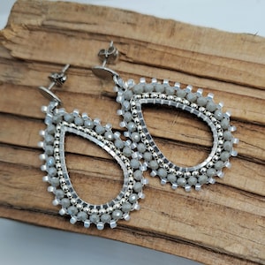 May include: A pair of silver teardrop-shaped earrings with a beaded design. The earrings are made with small, silver beads and have a silver post.