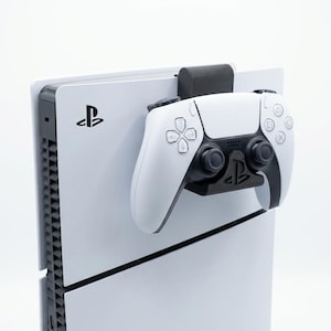 May include: A white PlayStation 5 console with a black controller holder and a white controller attached. The controller has black accents and the PlayStation logo is visible on the console.