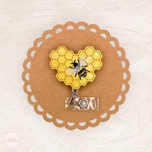 May include: A yellow heart-shaped badge holder with a bee and honeycomb design. The badge holder is attached to a retractable badge reel.