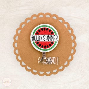 May include: A white badge reel with a red and green watermelon design. The watermelon has the text "Hello Summer" on it.