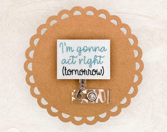 May include: A white badge reel with the text "I'm gonna act right (tomorrow)" in blue script. The badge is attached to a clear plastic reel with a metal clip. The badge is on a brown, scalloped-edge background.