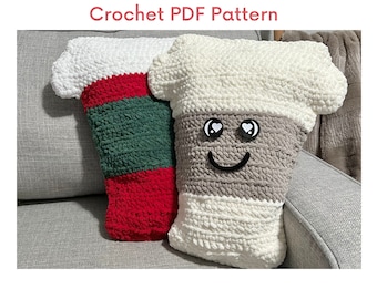 May include: Two crocheted coffee cup pillows, one with red, green, and white stripes and the other with gray, white, and black stripes and a smiling face with heart eyes.