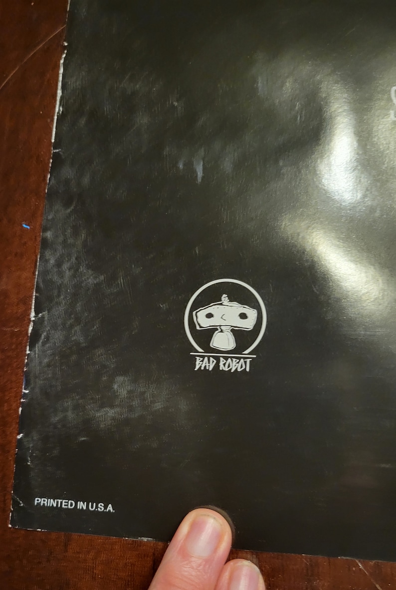 Puede incluir: Un p&oacute;ster en blanco y negro con el logotipo de Bad Robot. El logotipo es un robot blanco con un c&iacute;rculo a su alrededor. El texto "Bad Robot" est&aacute; debajo del robot. El p&oacute;ster tambi&eacute;n tiene el texto "PRINTED IN U.S.A." en la parte inferior.
