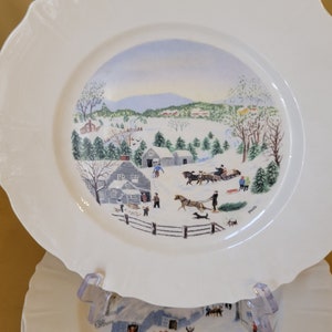 Puede incluir: Un juego de cuatro platos de cer&aacute;mica blanca con una escena de invierno pintada en ellos. La escena representa un paisaje nevado con casas, &aacute;rboles y personas. Los platos tienen un borde festoneado y son perfectos para una cena navide&ntilde;a.