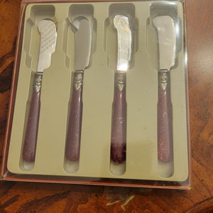Puede incluir: Juego de cuatro cuchillos de mantequilla de plata con mangos burdeos. Los cuchillos est&aacute;n en una caja de pl&aacute;stico transparente con fondo blanco. La caja tiene el texto "Stainless Dishwasher Safe Made in Italy Dish Washer Safe" impreso en ella.