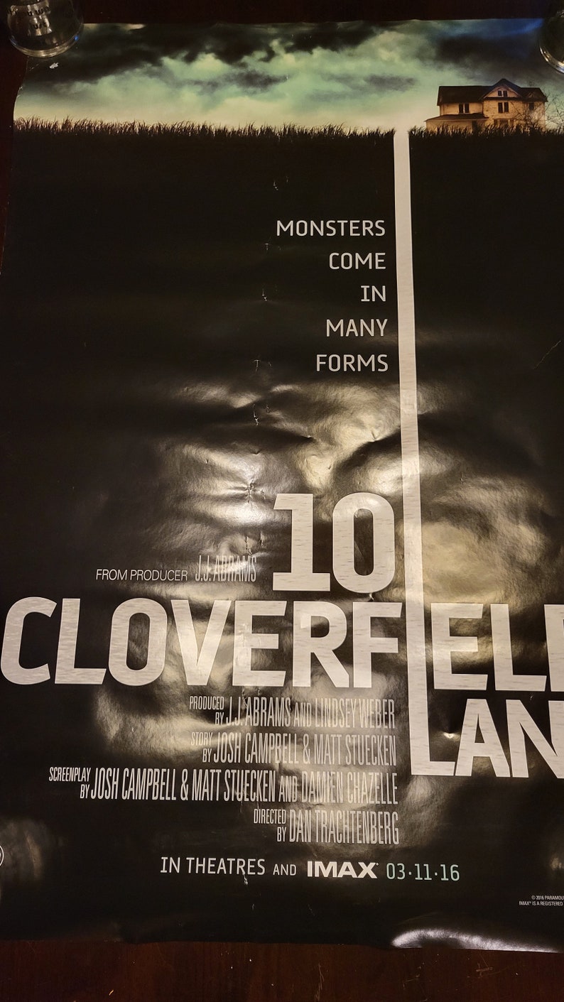 Puede incluir: Un p&oacute;ster de pel&iacute;cula en blanco y negro para la pel&iacute;cula "10 Cloverfield Lane". El p&oacute;ster presenta el t&iacute;tulo de la pel&iacute;cula en letras blancas grandes, con el lema "Los monstruos vienen en muchas formas" en letras blancas m&aacute;s peque&ntilde;as. El p&oacute;ster tambi&eacute;n presenta una peque&ntilde;a imagen de una casa en el fondo.