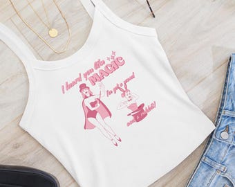 May include: White tank top with a pink graphic of a magician and a rabbit, with the text "I heard you like MAGIC, I've got a wand, and a rabbit!" Gold necklace and sunglasses are visible.
